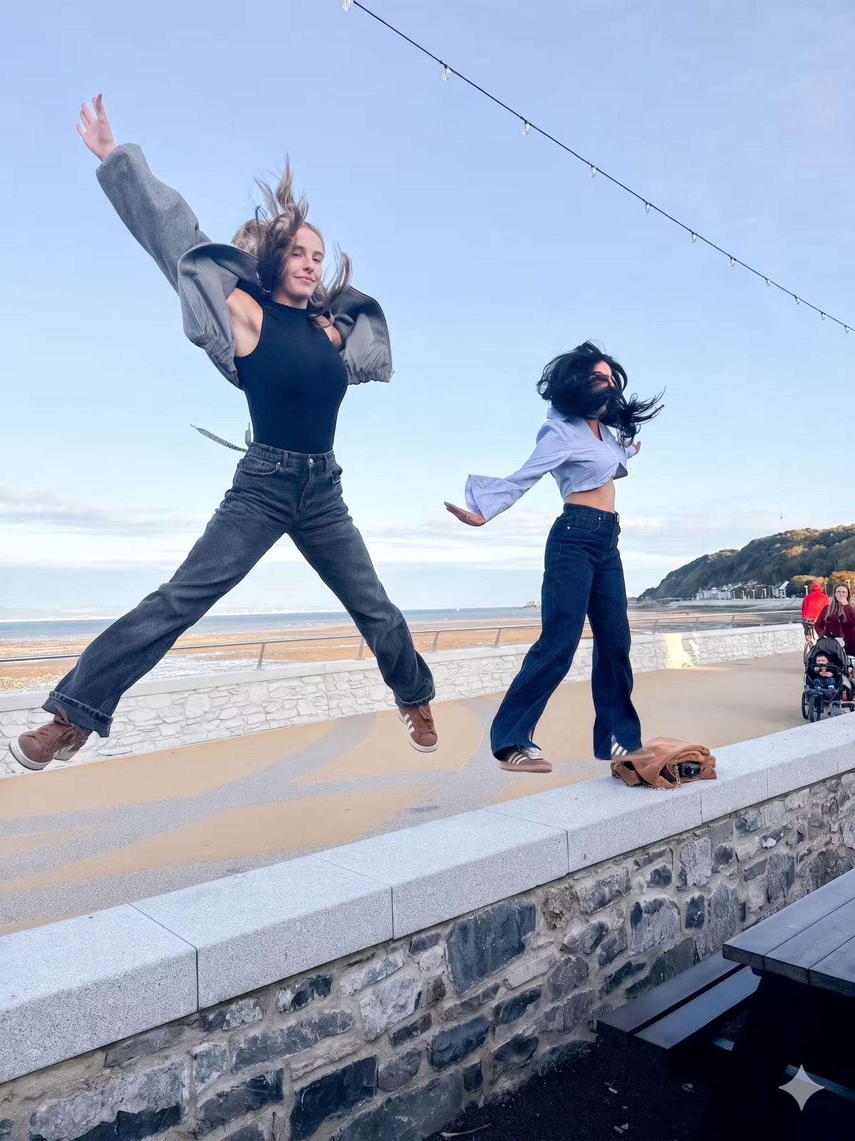 Two people jumping off a stone wall at a beach during a seaside team building activity.