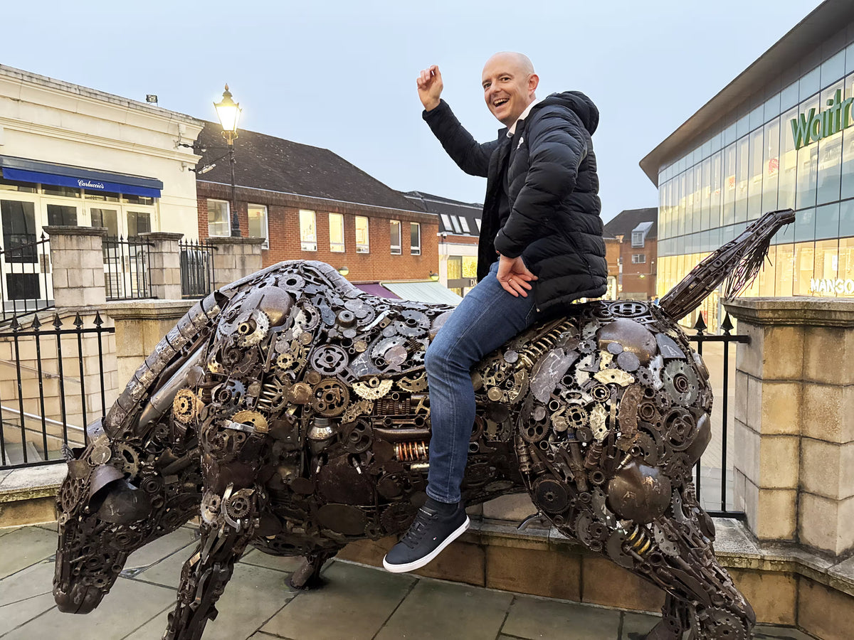 A man sitting on a large metallic bull sculpture during an urban team building task.