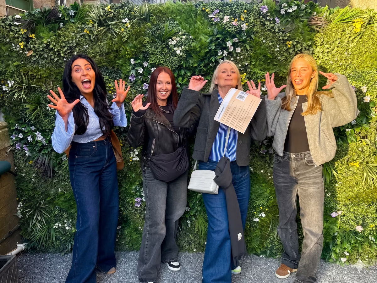 Four team members waving excitedly in front of a lush green ivy wall.