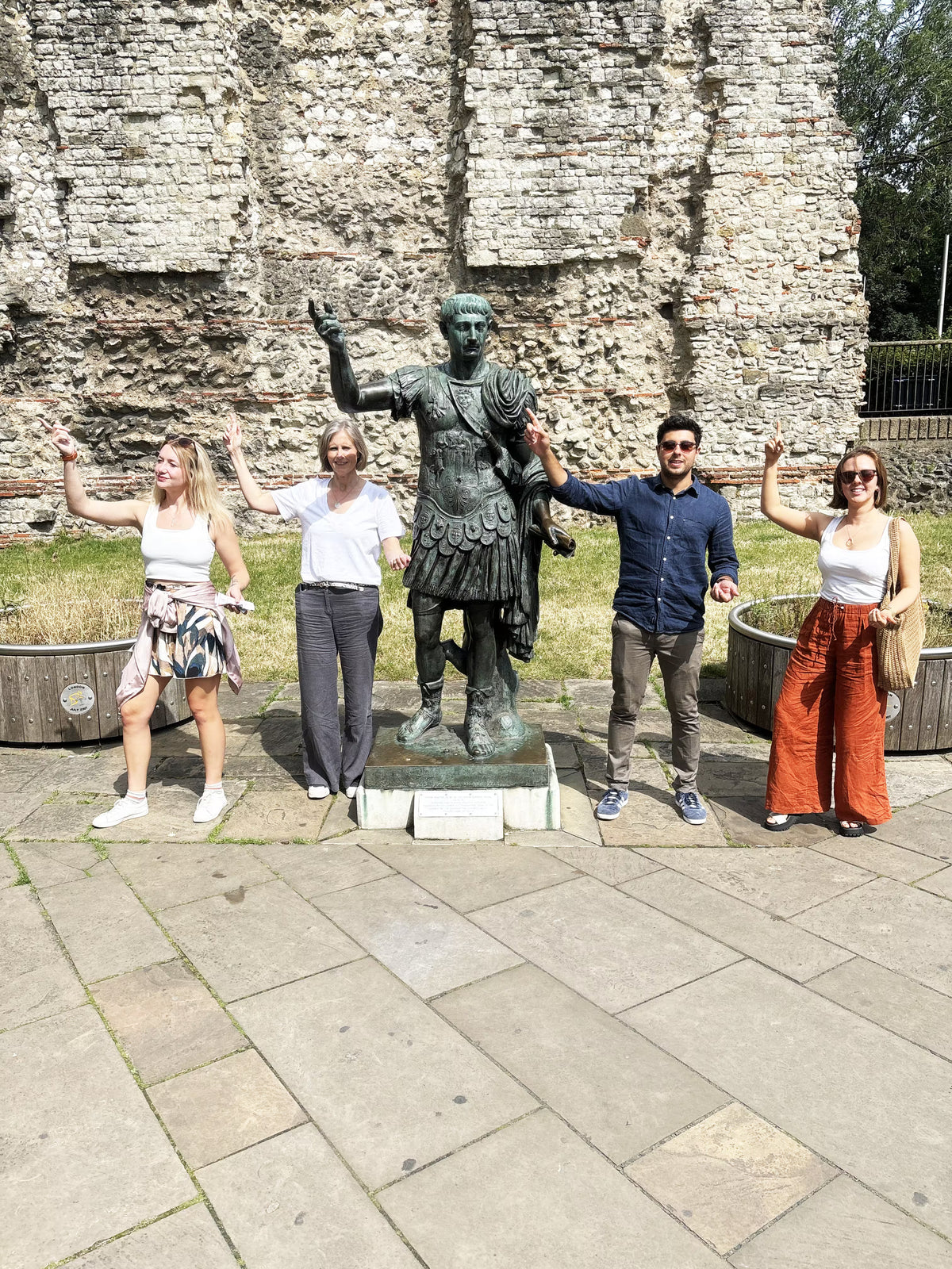 A group of four people posing in front of a bronze statue and ancient stone wall.