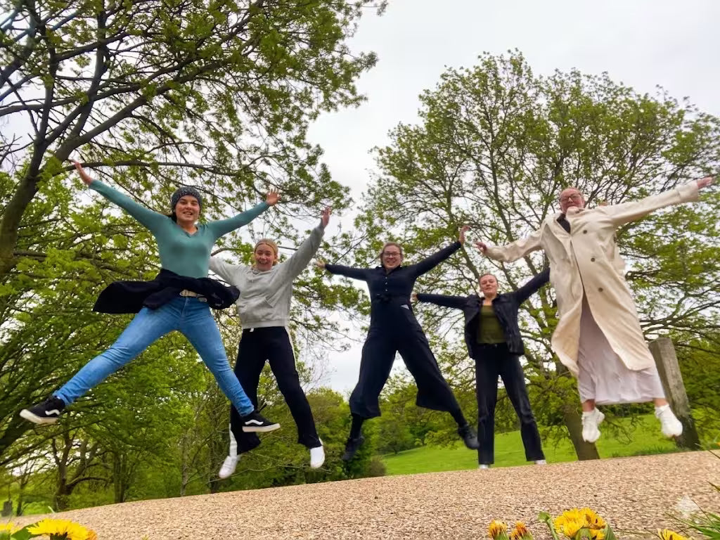 A group of coworkers jumping together in a wooded park area for a team spirit photo.