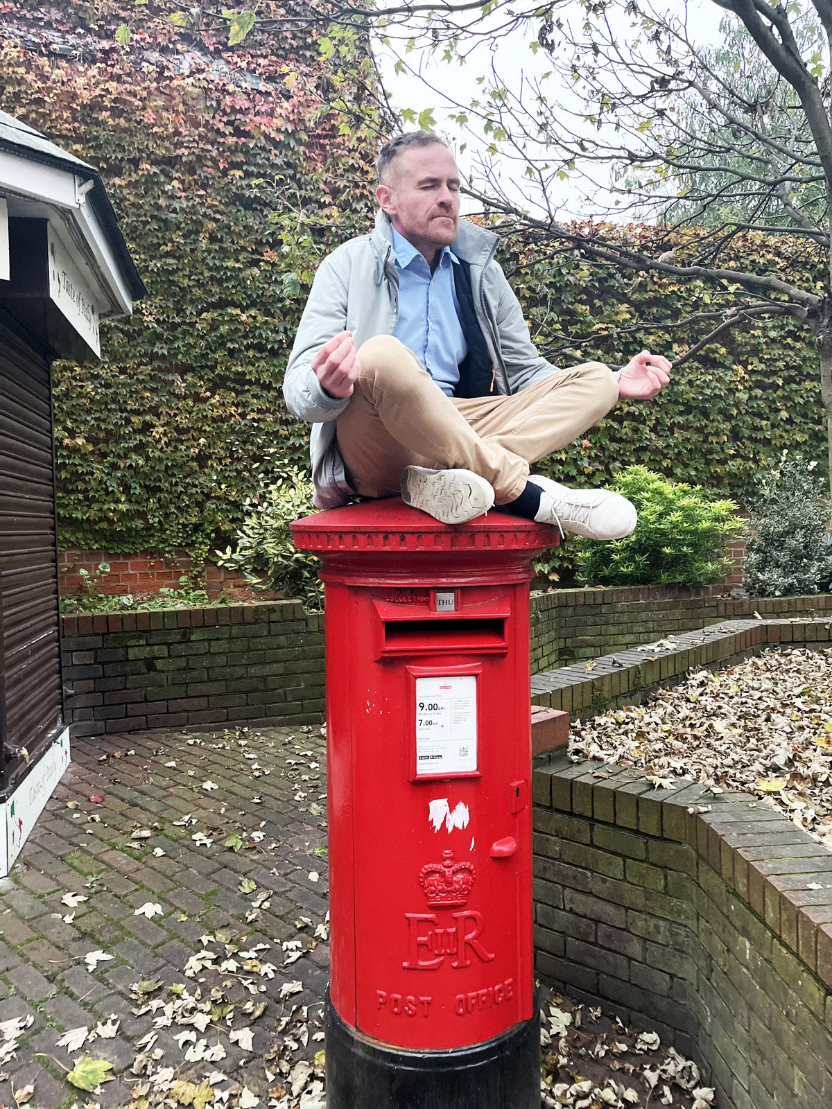 A man sitting in a meditation pose on top of a classic red pillar post box.