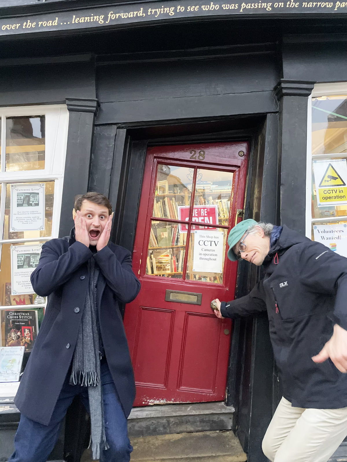 Two people making surprised faces in front of a historic red wooden door.