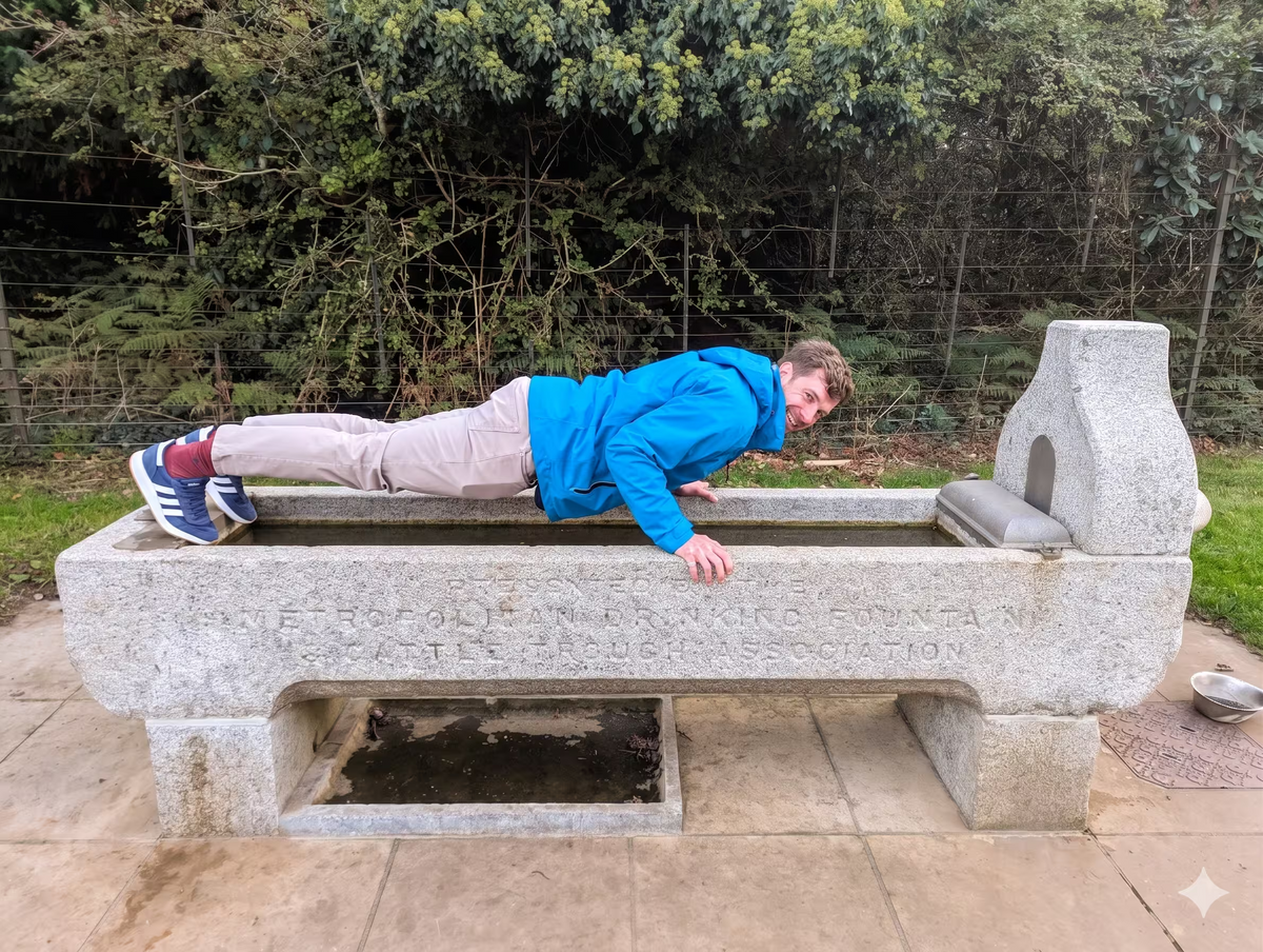 A person performing a push-up or plank on a historic stone trough in a park.